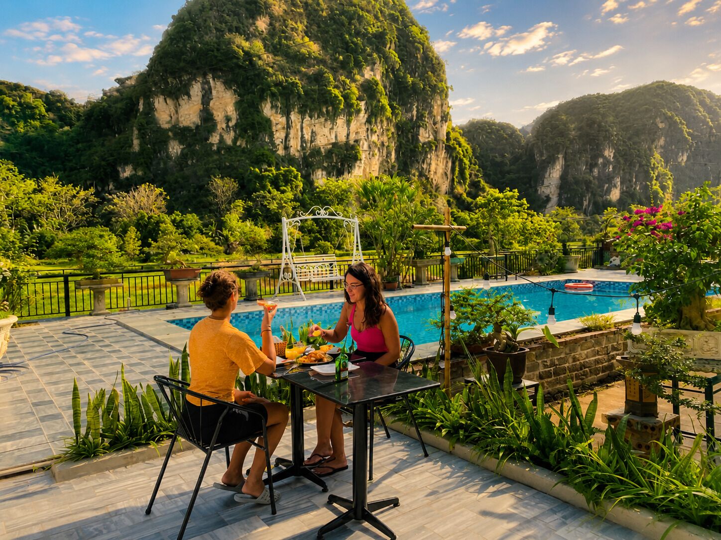 Ein Poolbereich mit Tisch und Stühlen, umgeben von üppiger Vegetation und Blick auf eine gebirgige Landschaft.