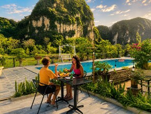 A poolside area with a table and chairs, surrounded by lush greenery and a view of a mountainous landscape. - Tam Coc AppA House (Nam Hoa Lu)