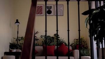 A living room with a sofa, red cushions, and multiple potted plants.