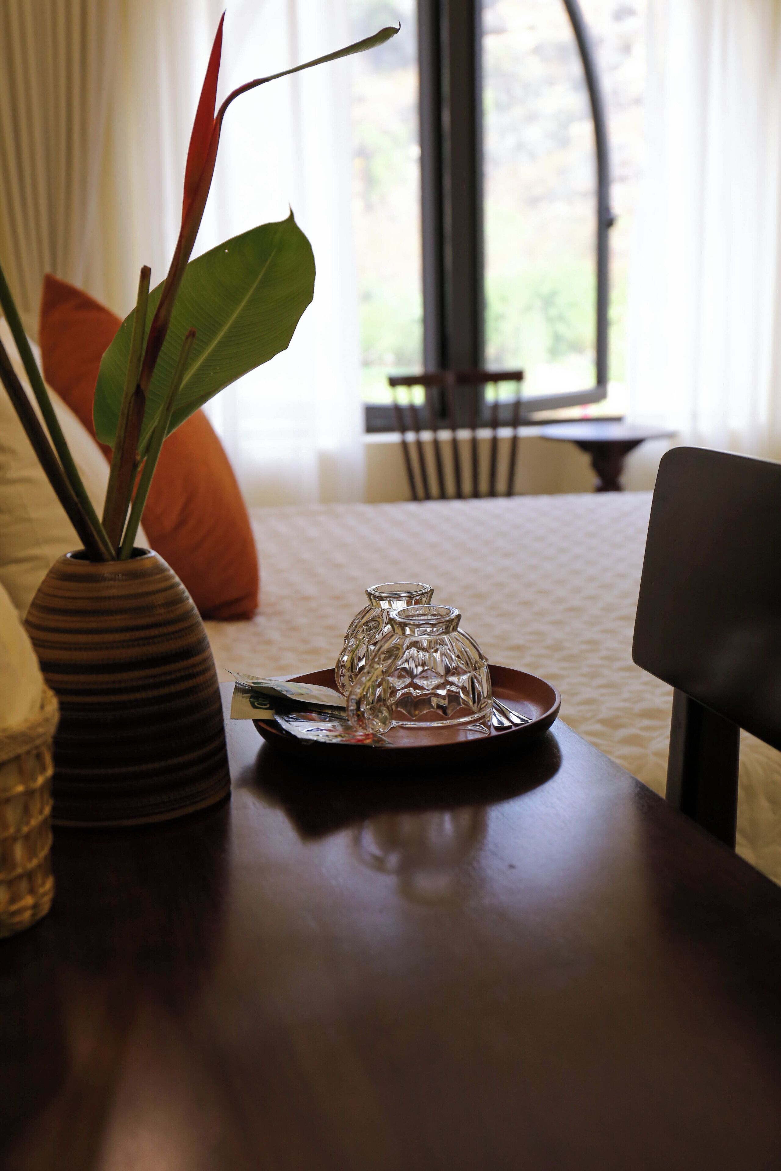 A dining table with a vase and a glass pitcher, a chair, and a window with curtains.