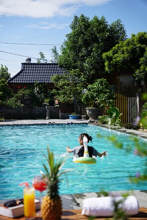A swimming pool with a person on a float, surrounded by greenery and a building with a tiled roof. - Tam Coc AppA House (Nam Hoa Lu)