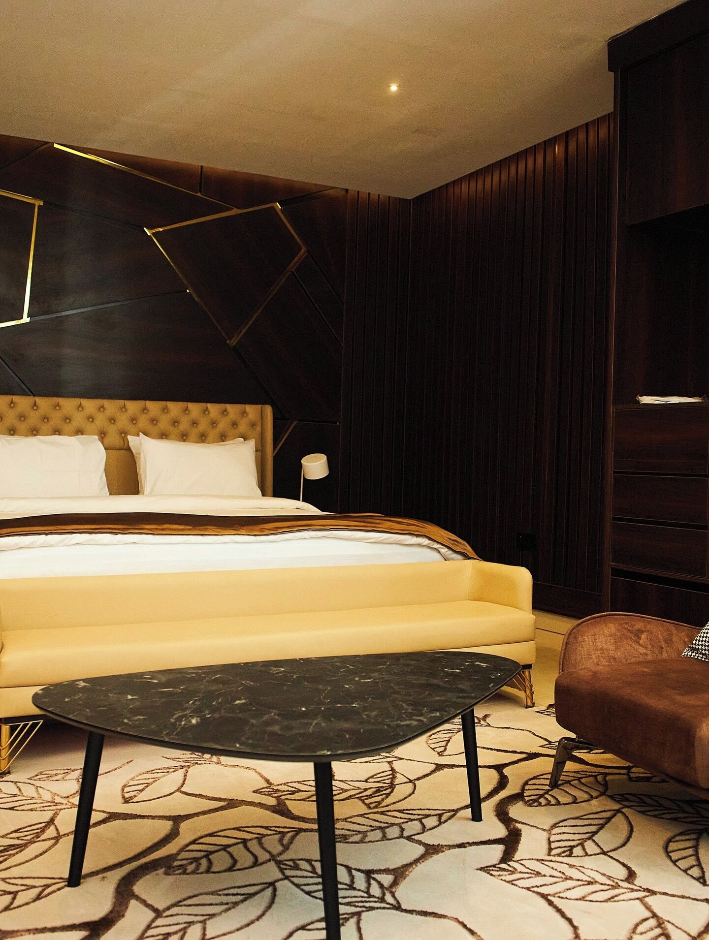 Een slaapkamer met een bed, een nachtkastje, een stoel en een kamerbreed tapijt met dessin.