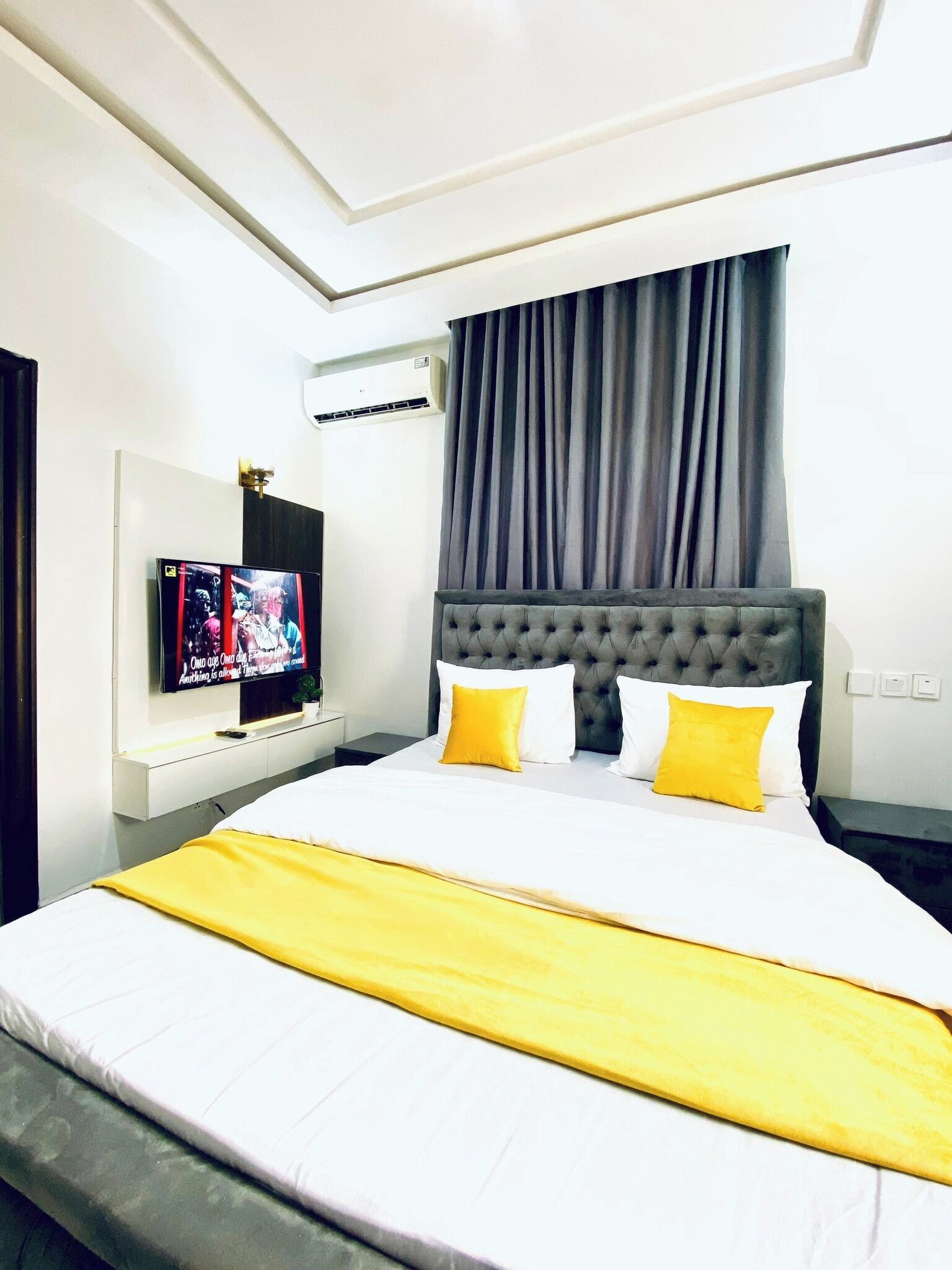 Ein Hotelzimmer mit einem großen Bett, einem Flachbildfernseher, einer wandmontierten Klimaanlage und einem Fenster mit Vorhängen.