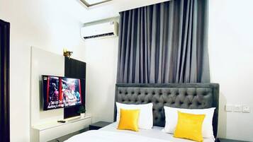 Ein Hotelzimmer mit einem großen Bett, einem Flachbildfernseher, einer wandmontierten Klimaanlage und einem Fenster mit Vorhängen.
