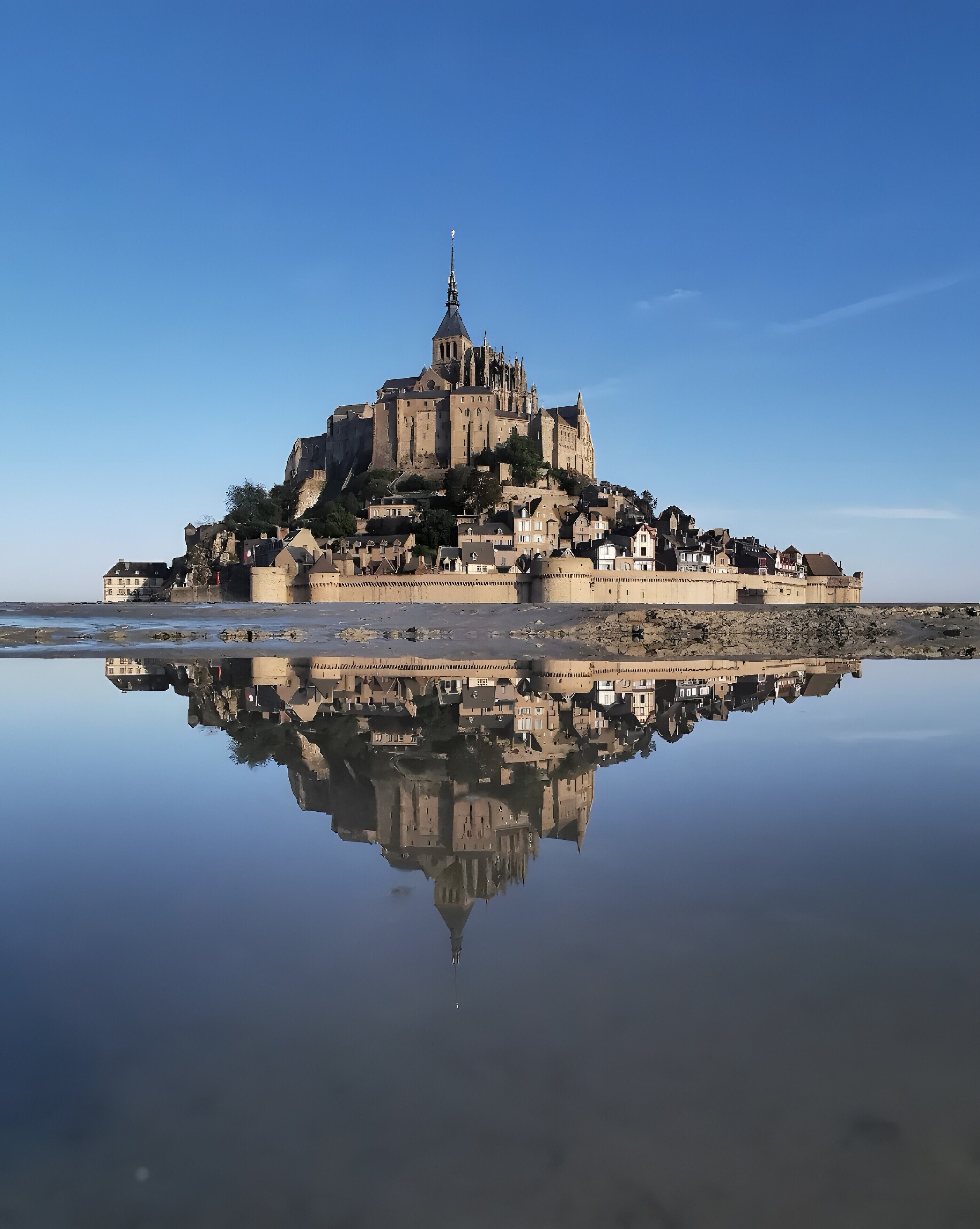 A historic castle on a rocky island with a clear reflection in calm water.