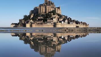 A historic castle on a rocky island with a clear reflection in calm water.