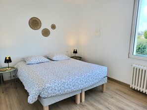 Une chambre à coucher comprenant un lit, deux tables de chevet, des éléments de décoration murale, une fenêtre et un radiateur.
