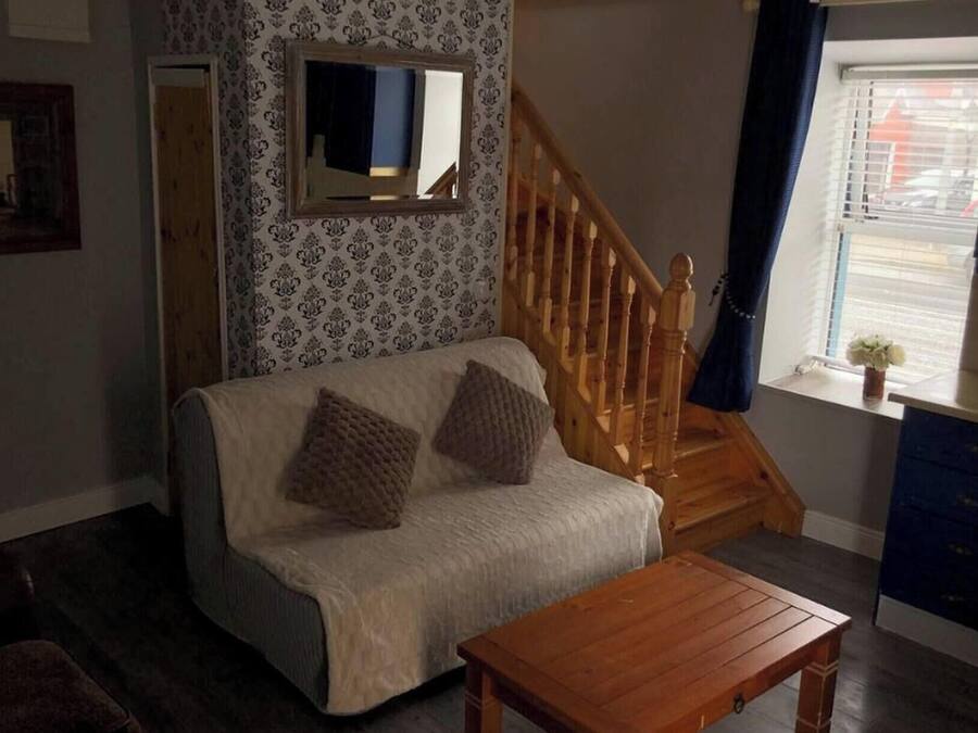 Un salon comprenant un canapé, une table basse en bois, un miroir, un escalier et une fenêtre avec des stores.