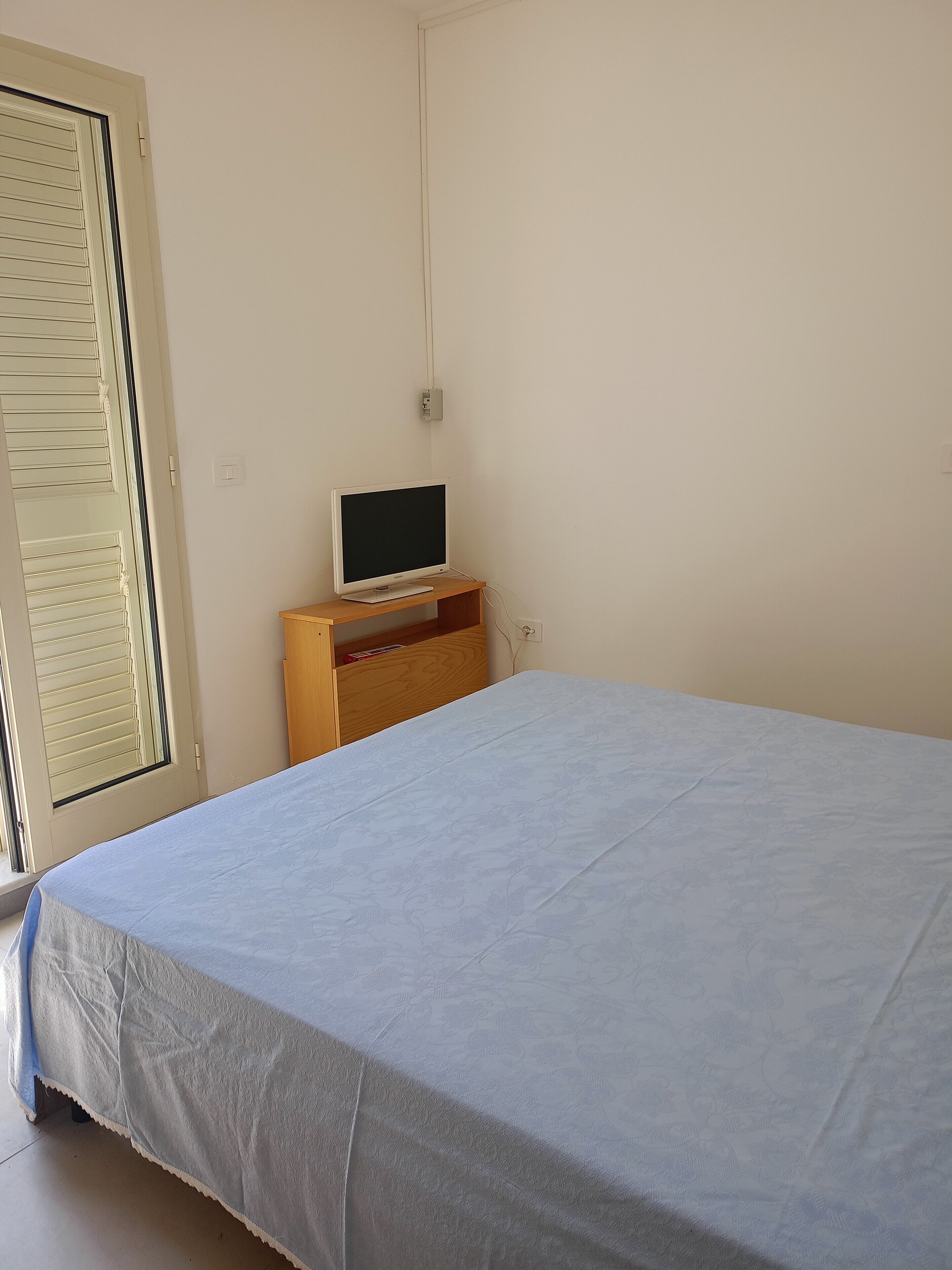 Una camera da letto con un letto, una televisione su un mobile in legno, una finestra con persiane e una porta.