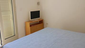 Una camera da letto con un letto, una televisione su un mobile in legno, una finestra con persiane e una porta.
