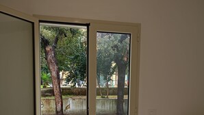 A bedroom with a bed, a TV on a wooden stand, and a sliding glass door leading to an outdoor area with trees and a street. - Casa Vista Villa Room with Wi-Fi and Air Conditioning (Supersano)