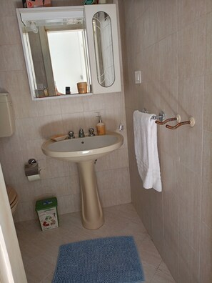 Une salle de bain avec un lavabo sur colonne, un miroir au-dessus, un porte-serviettes et un tapis bleu sur le sol.