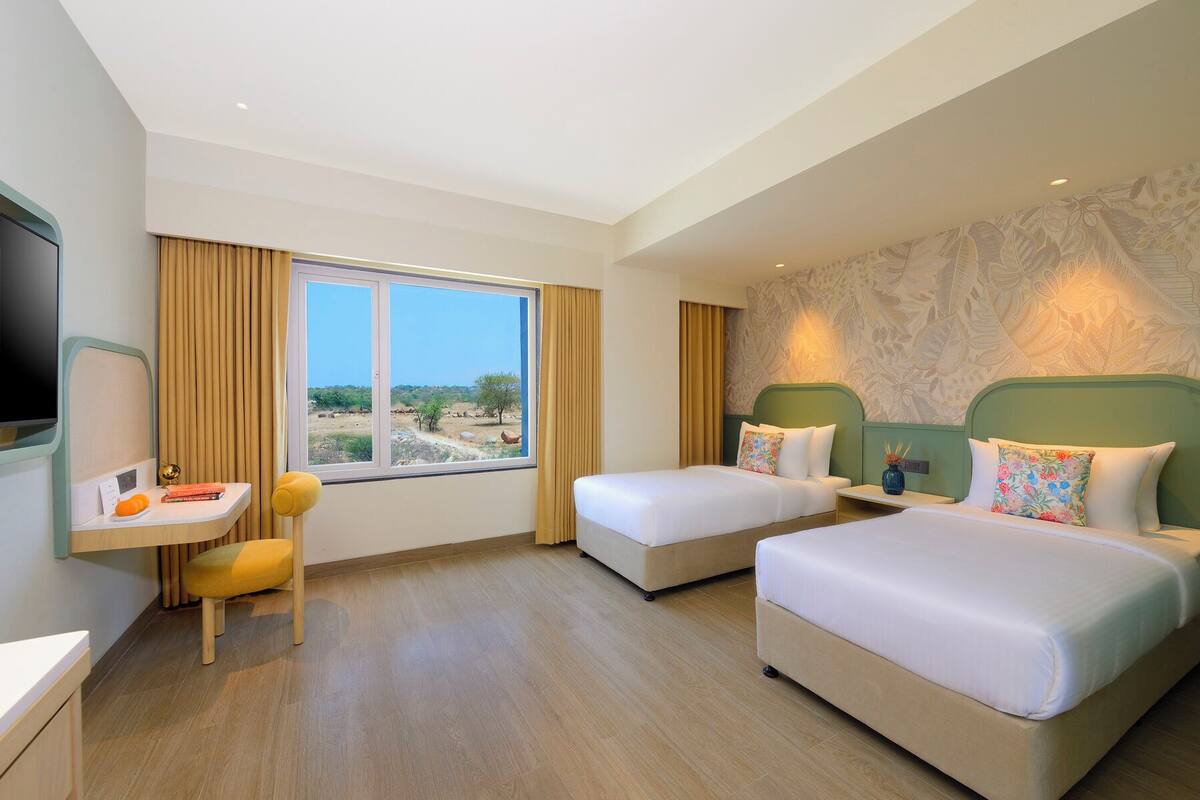 A hotel room with two beds, a desk, a chair, and a TV.