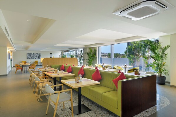 Un ristorante moderno con un divano verde, sedie e tavoli in legno.