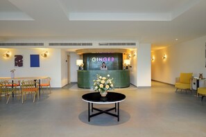 A reception area with a green counter, a receptionist, and a round table with a vase of flowers. - Ginger Hyderabad Genome Valley (Shamirpet)