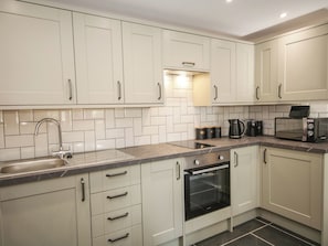 A modern kitchen with white cabinets, a stainless steel sink, a built-in oven, and a microwave. - Sun Trevor Barns 3 (Llangollen)