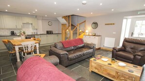 A living room with a sofa, a coffee table, and a dining area with a table and chairs. - Sun Trevor Barns 2 (Llangollen)