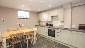 A modern kitchen with white cabinets, a wooden dining table, and a tiled floor. - Sun Trevor Barns 2 (Llangollen)