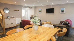 A dining area with a wooden table, chairs, a vase with flowers, a television, and a sofa with a red blanket. - Sun Trevor Barns 2 (Llangollen)