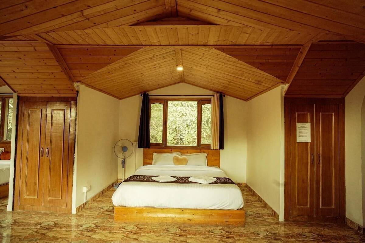 A bedroom with a wooden ceiling, a bed with white bedding, a window with curtains, and a fan.