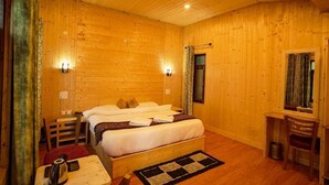 A wooden-paneled room with a bed, bedside table, and a desk with a chair. - Royal Stay In The Nature's Lap (Shoghi)