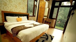 A bedroom with a large bed, a wooden headboard, a wardrobe, a desk, and a balcony with a view of greenery. - Royal Stay In The Nature's Lap (Shoghi)