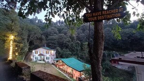 A house with a green roof, surrounded by trees and a sign that reads 'YOU HAVE REACHED AT YOUR DESTINATION.' - Royal Stay In The Nature's Lap (Shoghi)