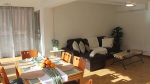 Un salon avec un canapé, une table à manger ornée de fruits, une petite table avec une plante et un ventilateur de plafond.