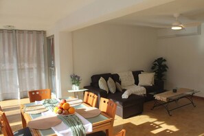 A living room with a sofa, a dining table with fruit, a small table with a plant, and a ceiling fan. - Agua Azul · Reformado · 5 Pax · Parking/wifi (Benidorm)