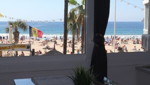Vista a la playa desde una ventana con una bandera, palmeras y un cartel que dice 'Las Jaras'.