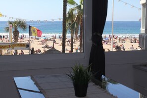 Blick auf einen Strand aus einem Fenster, mit einer Flagge, Palmen und einem Schild für 'Las Jaras'.