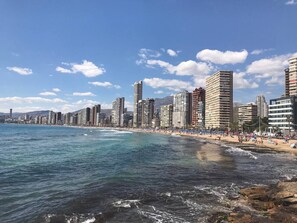 Eine Küstenlandschaft mit hohen Gebäuden, einem Strand und blauem Himmel.
