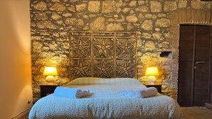 Ein Bett mit strukturierter Decke, zwei Nachttischlampen, eine Steinwand und eine Holztür.