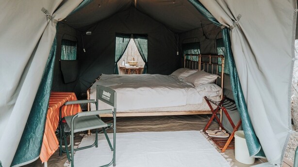 A tent with a bed, a chair, a table, and a hanging light fixture.