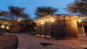 A stone-paved outdoor area with a thatched structure and string lights.