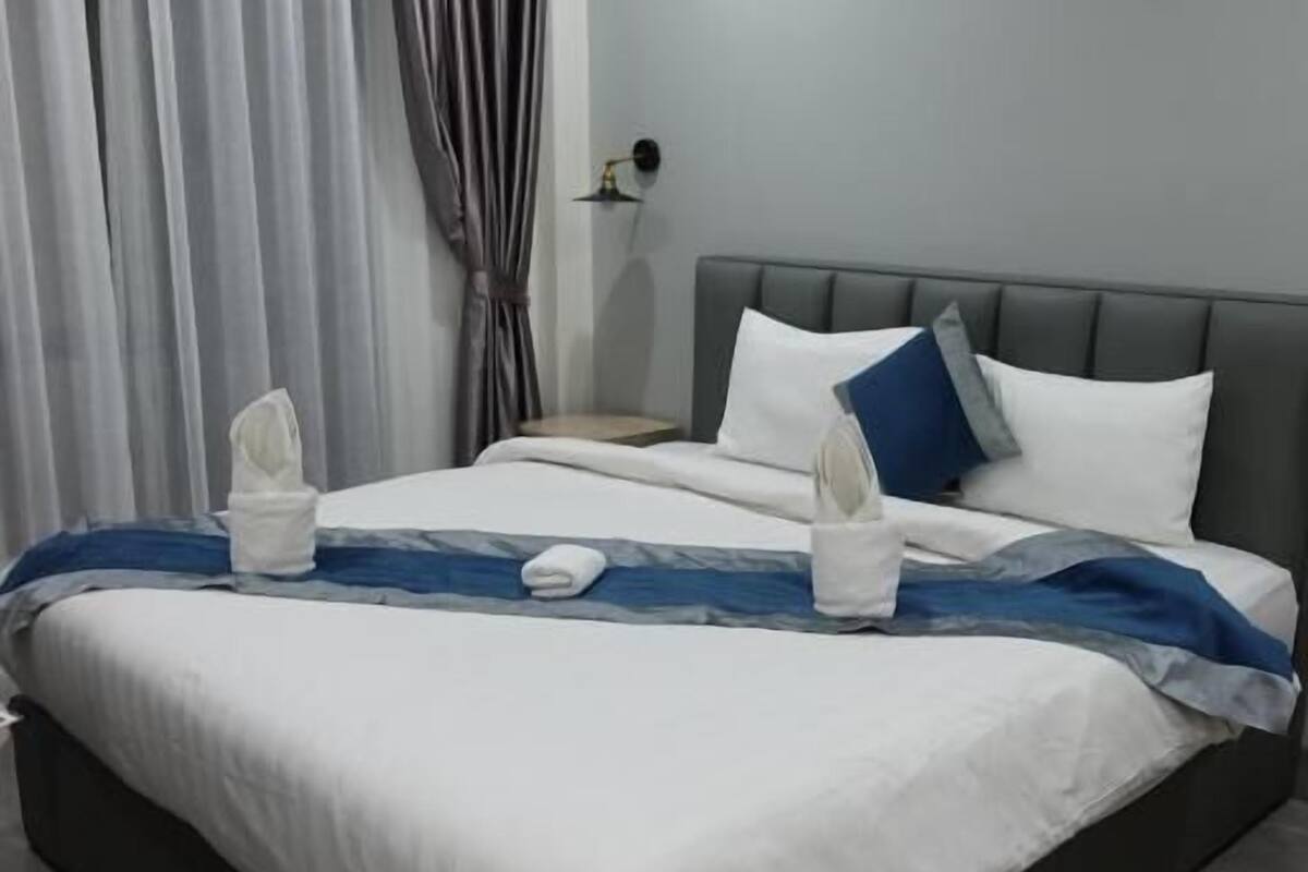 Une chambre d’hôtel moderne avec un grand lit, des rideaux gris, une table de chevet et une petite table de nuit.