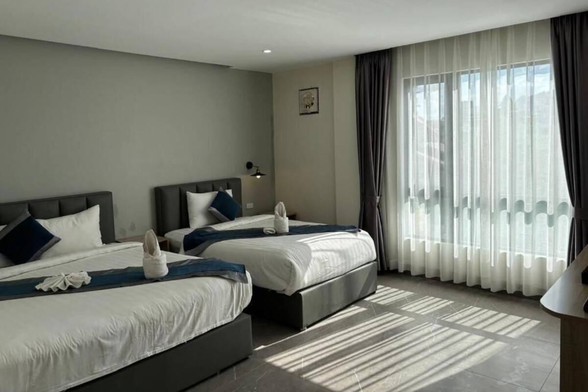 Une chambre d’hôtel avec deux lits, une grande fenêtre avec des rideaux légers et un design moderne.