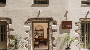 A building with a sign reading 'ETEÓN' and a doorway leading to an interior space with a table and chairs. - Eteon Living Suites (Chania)