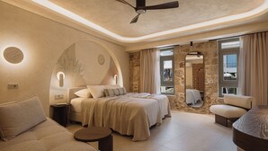 A bedroom with a bed, two bedside tables, a round table, a sofa, a ceiling fan, and a large mirror. - Eteon Living Suites (Chania)