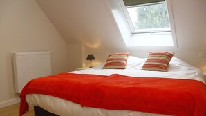 A bedroom with a sloped ceiling, a skylight, a radiator, a bedside lamp, and a bed with a red blanket and striped pillows. - Holiday home for 8 people on a renovated farm (sijsele)