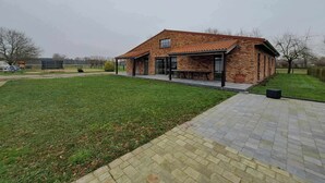 Ein modernes Backsteinhaus mit überdachter Terrasse, einem Rasen und einem gepflasterten Weg.