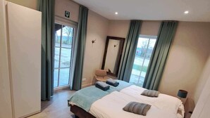 Ein Hotelzimmer mit einem großen Bett, einem Sessel, einem Schreibtisch, einem Spiegel und einem Fenster mit Vorhängen.