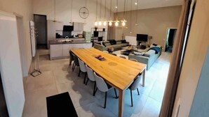 Eine moderne Küche mit Essbereich, ein Wohnzimmer mit Sofa und Fernseher sowie ein Flur, der zu einem weiteren Raum führt.