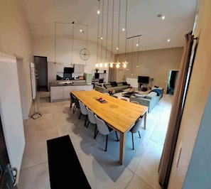 Eine moderne Küche mit Essbereich, ein Wohnzimmer mit Sofa und Fernseher sowie ein Flur, der zu einem weiteren Raum führt.