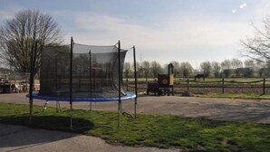 Ein Trampolin mit Sicherheitsnetz, einem umzäunten Bereich und einem Pferd im Hintergrund.