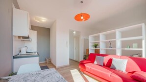 Una sala de estar moderna con un sofá rojo, una mesa de centro blanca y una zona de cocina con armarios y encimera.