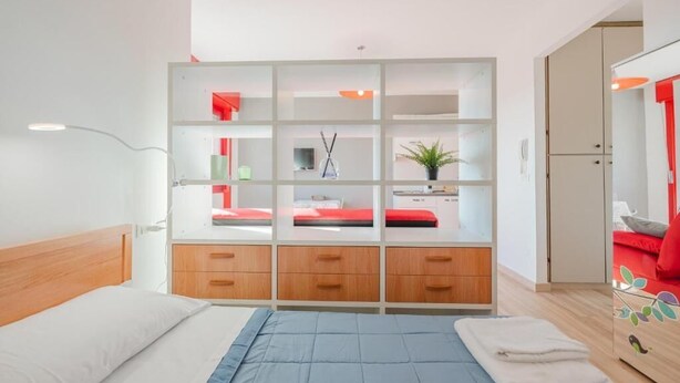 Un dormitorio con cama, armario con varios compartimentos, mesita de noche y espejo.