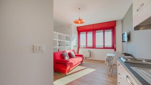 Un espacio habitable moderno con un sofá rojo, una zona de cocina y un ventanal con cortinas rojas.