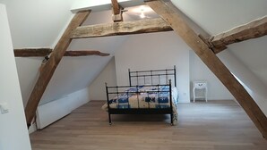 A room with a wooden ceiling, a bed with a patterned bedspread, and a small white cabinet.
