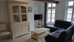 A living room with a black leather sofa, a white cabinet, a small white table, and a TV on a white stand.
